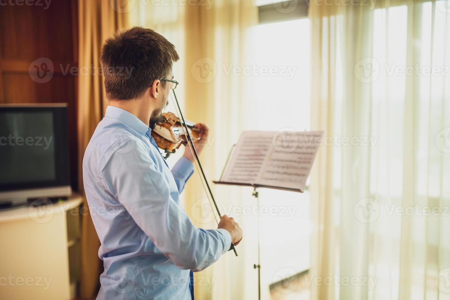 Man playing violin at home. He is cleaning his instrument. photo