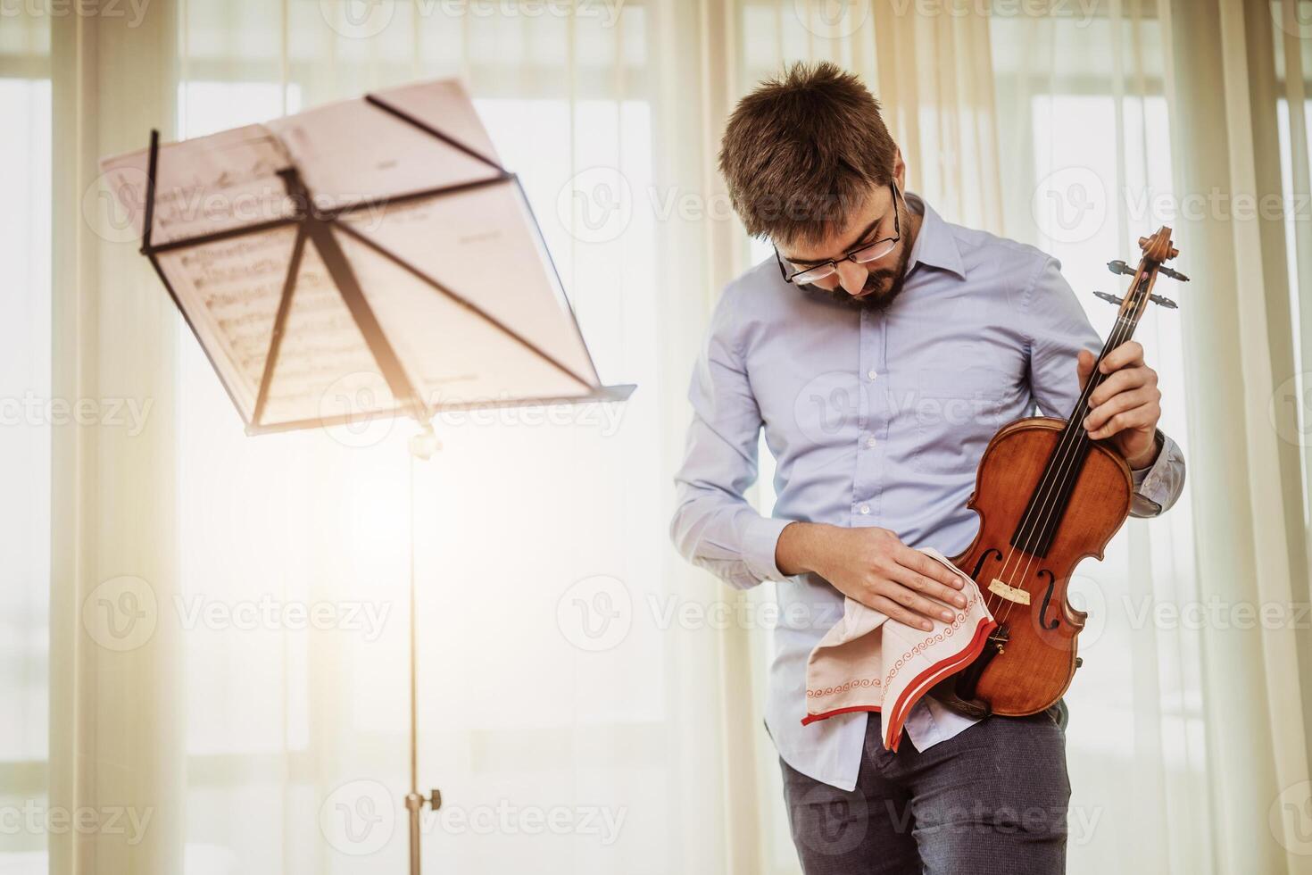 Man playing violin at home. He is cleaning his instrument. photo