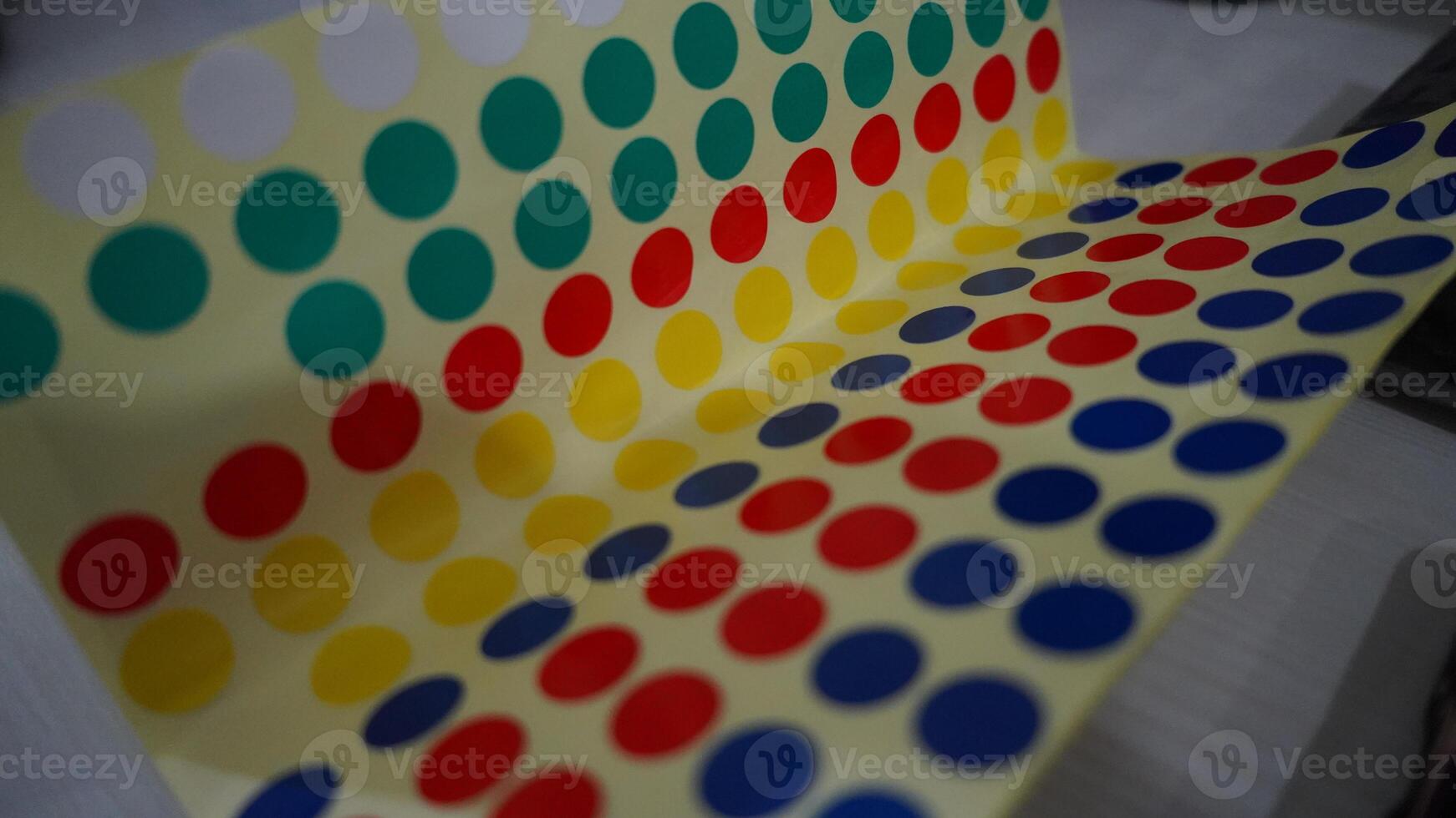 a sheet of square stickers with a colorful polka dot design. The stickers are arranged in a row on a clear plastic sheet. The background is yellow. photo