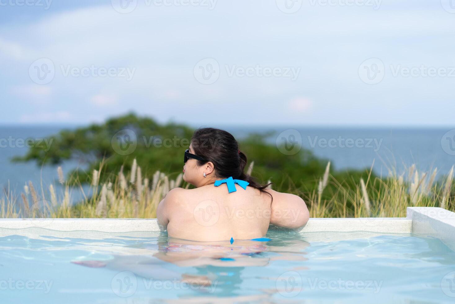 retrato de asiático más Talla hermosa mujer vistiendo bikini y en pie en nadando piscina mirando a Oceano mientras en dia festivo foto