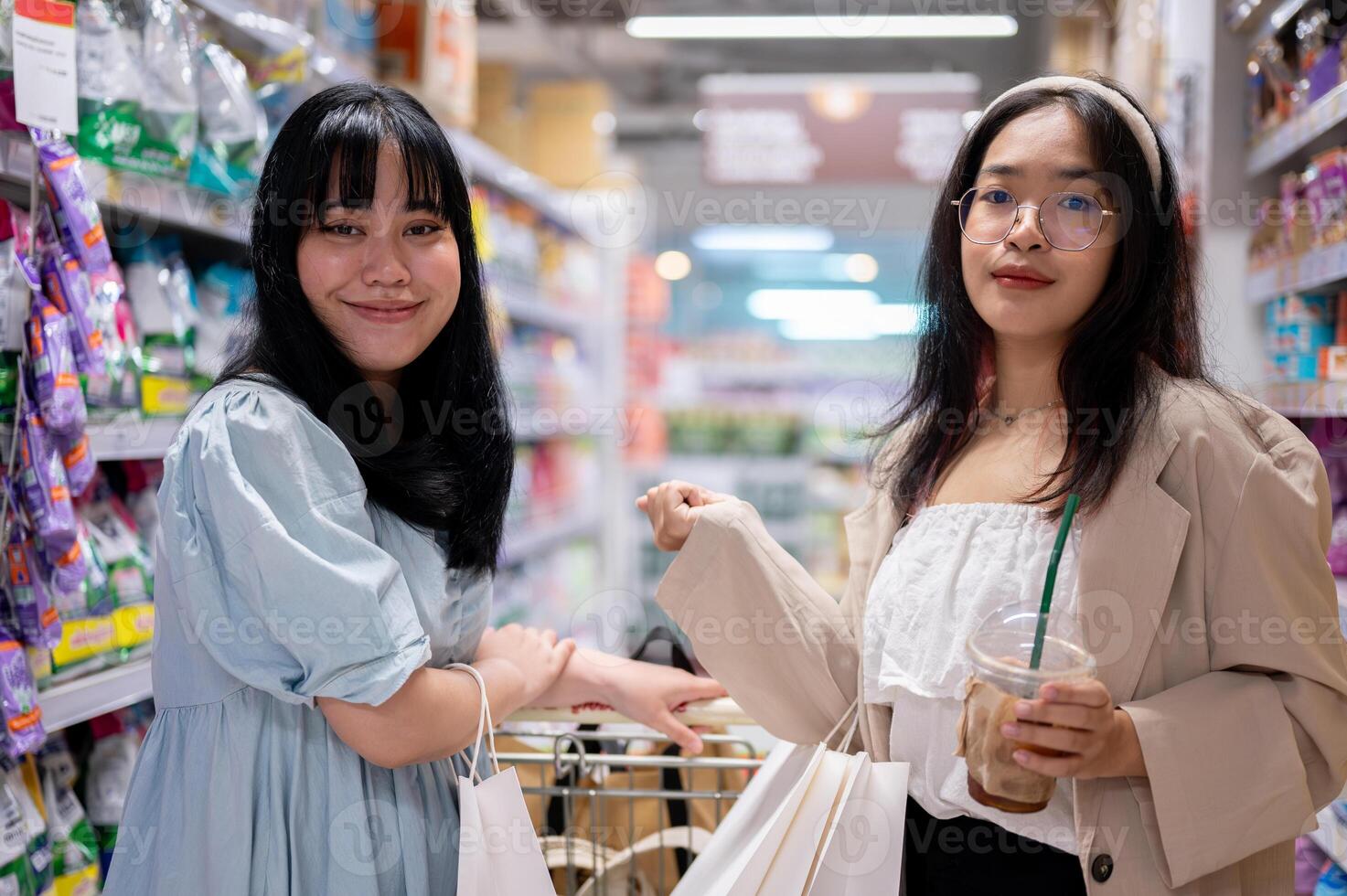 Two happy young Asian women shop together in a grocery store, walking with a shopping cart. photo
