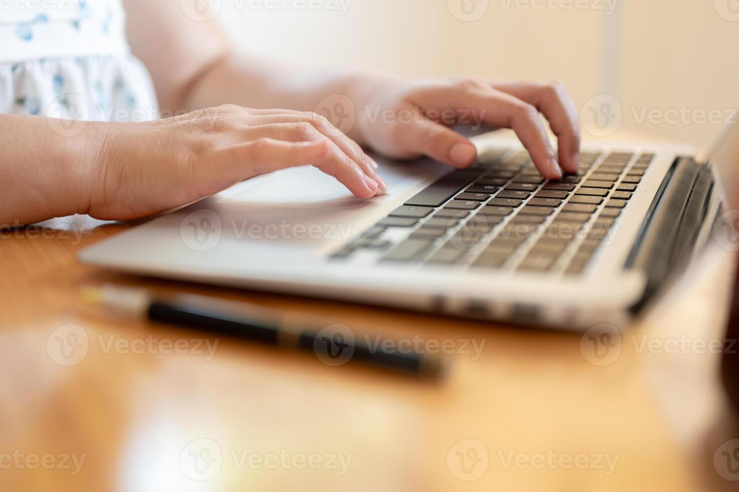 A close-up image of a woman using her laptop at a table indoors, typing on the laptop keyboard. photo
