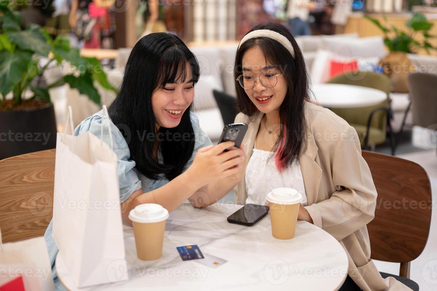 Two Asian female friends are enjoying talking while sitting together in a cafe in the shopping mall. photo