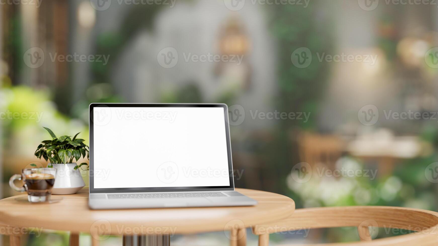 A white-screen laptop computer mockup is placed on a wooden table in a cafe on a sunny day. photo