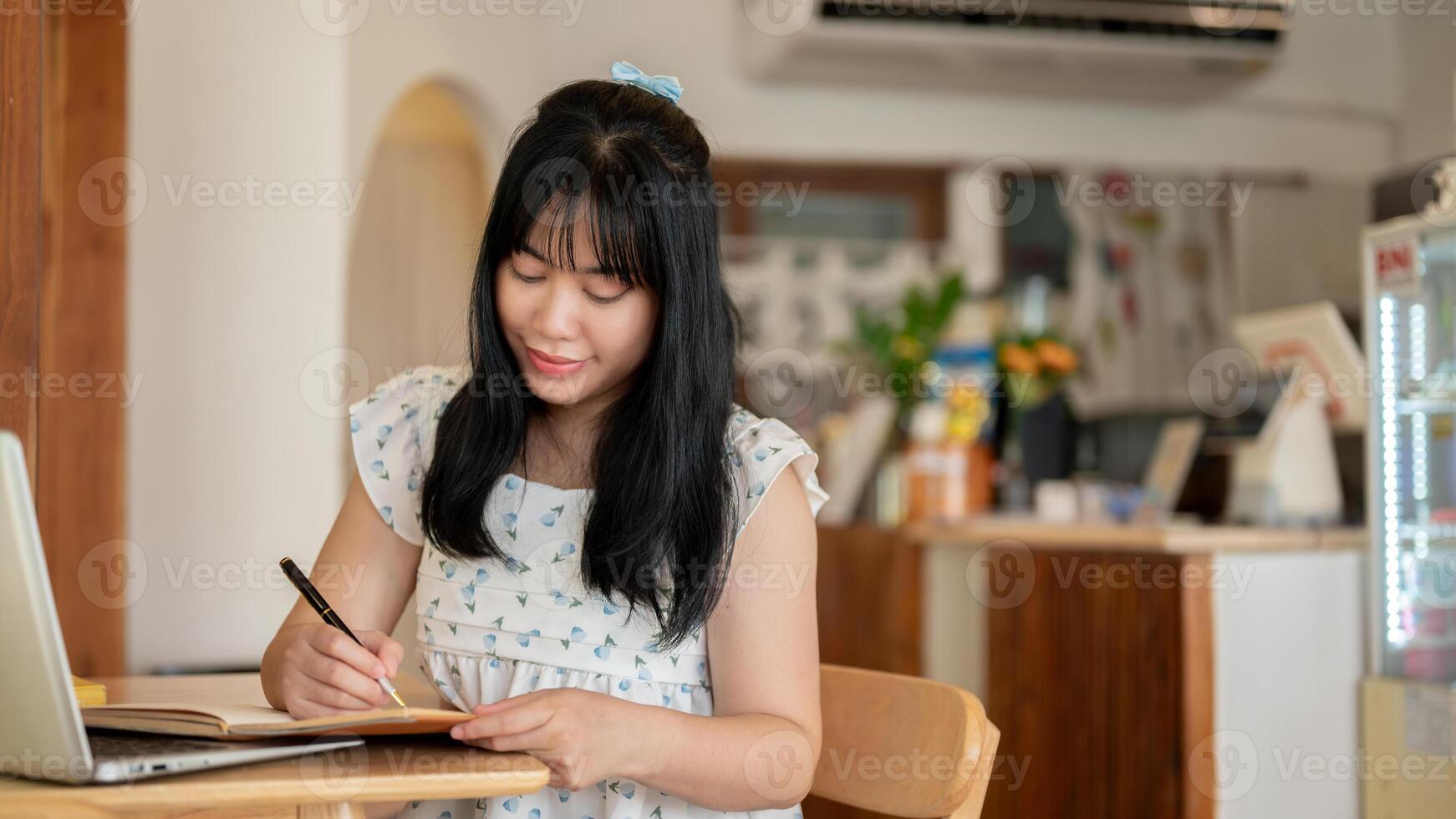 A beautiful Asian woman focusing on writing something in a notebook while sitting in a coffee shop. photo