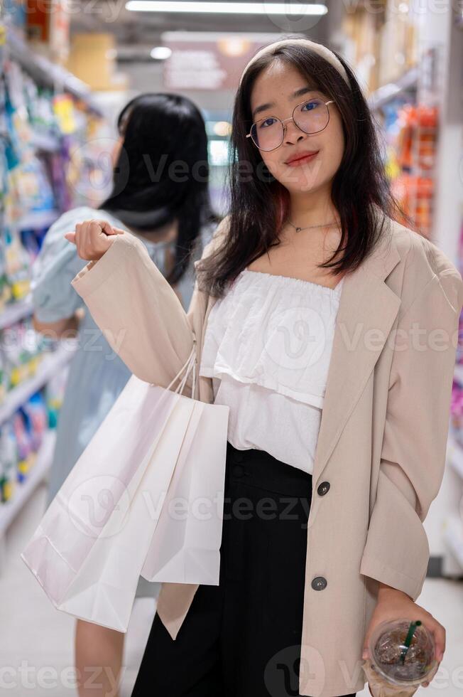A smiling Asian woman stands in a grocery aisle, holding shopping bags, shopping in a supermarket. photo