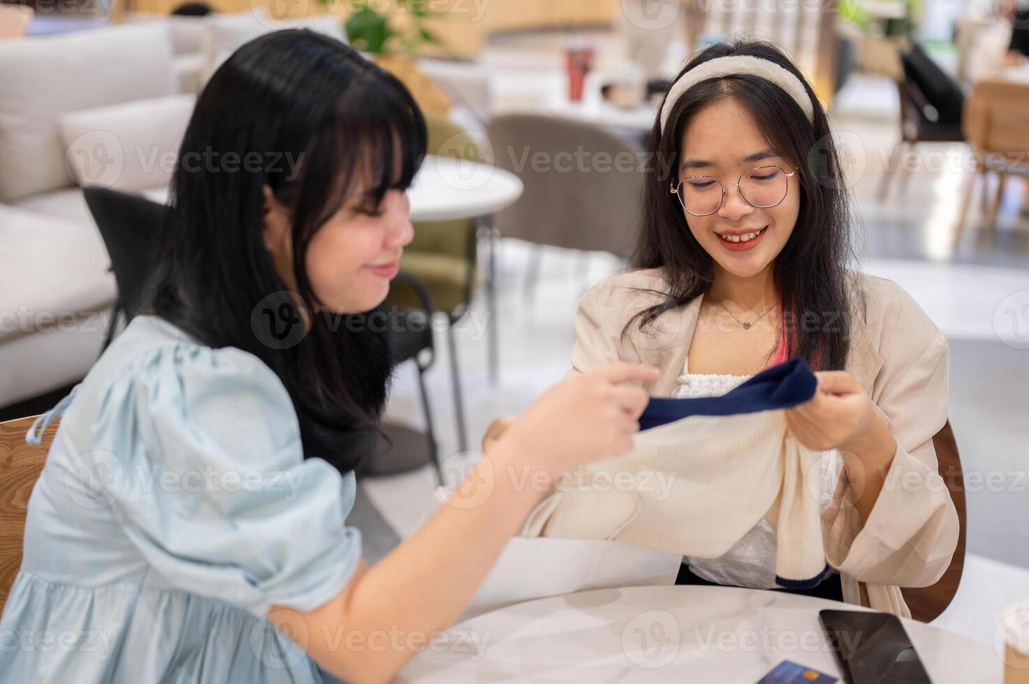 Two Asian women sit in a cafe at a mall, one excitedly showing off a new shirt to her friend. photo