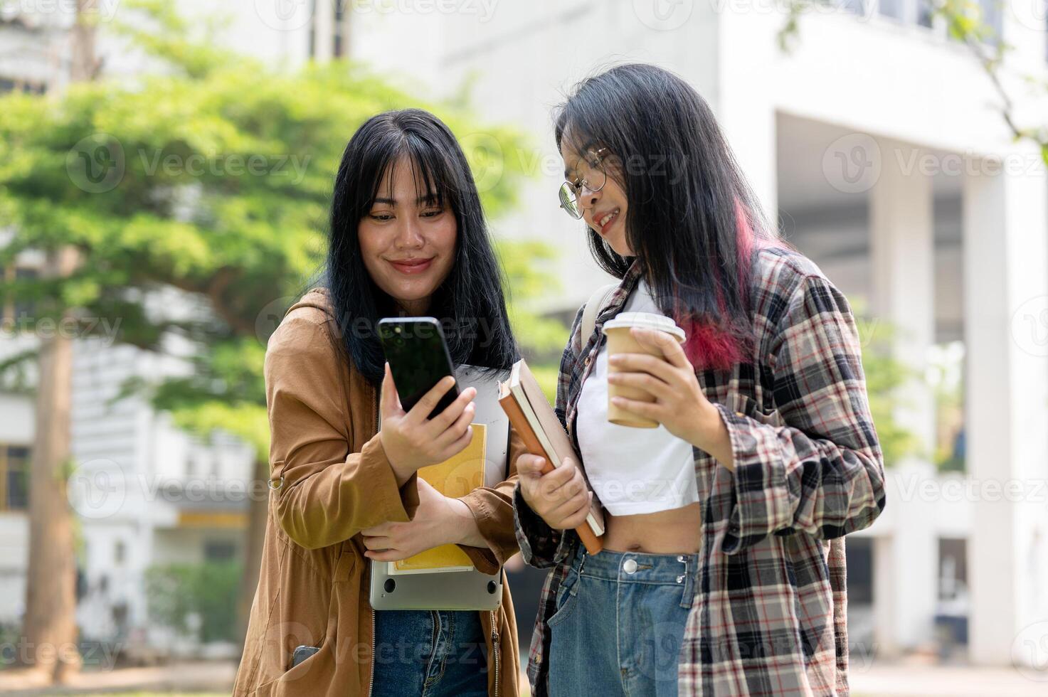 Two Asian female college students are standing together in the campus park, looking at a smartphone. photo