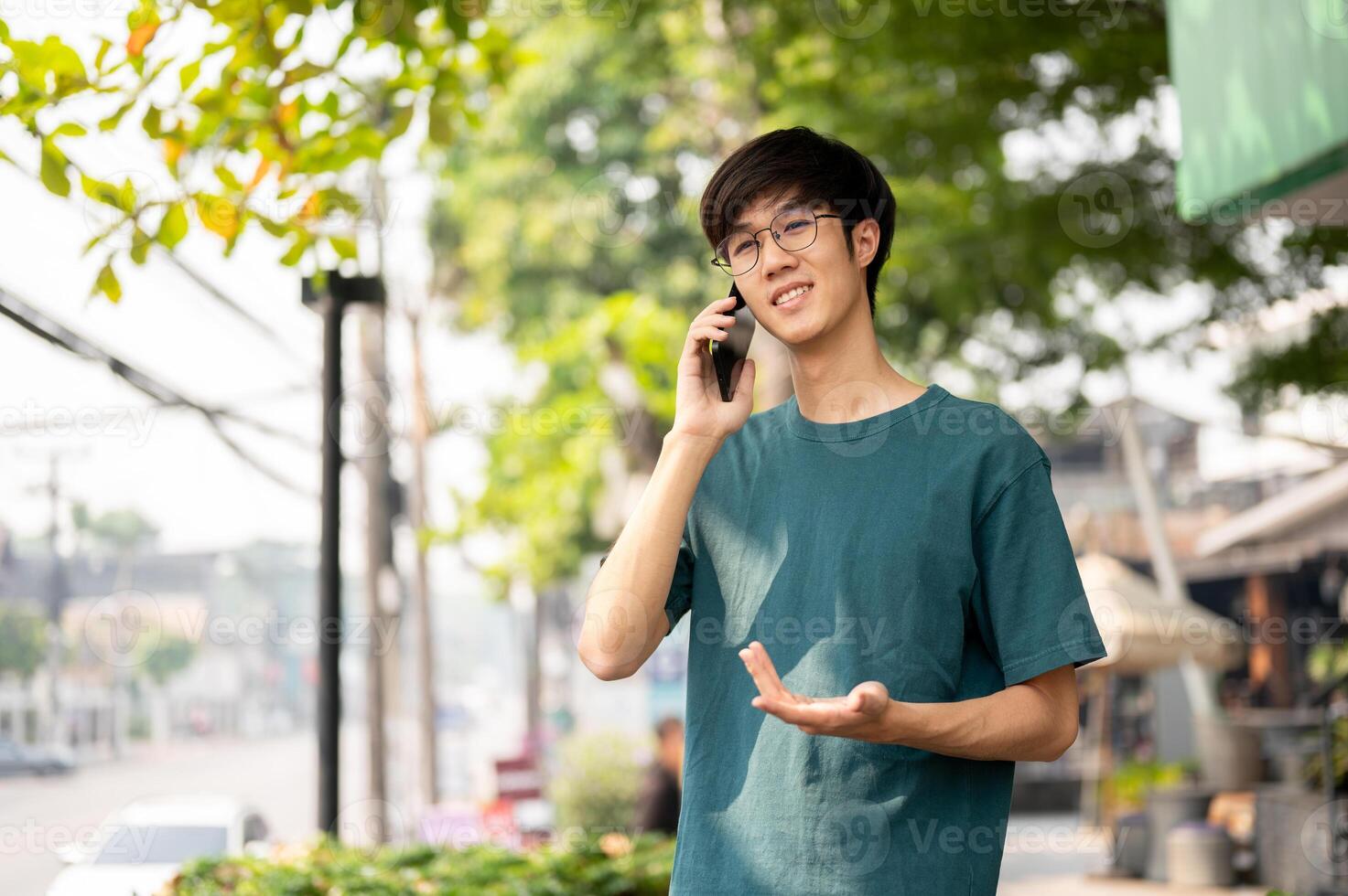 A young Asian man in casual wear is talking on the phone with someone while walking in the city. photo