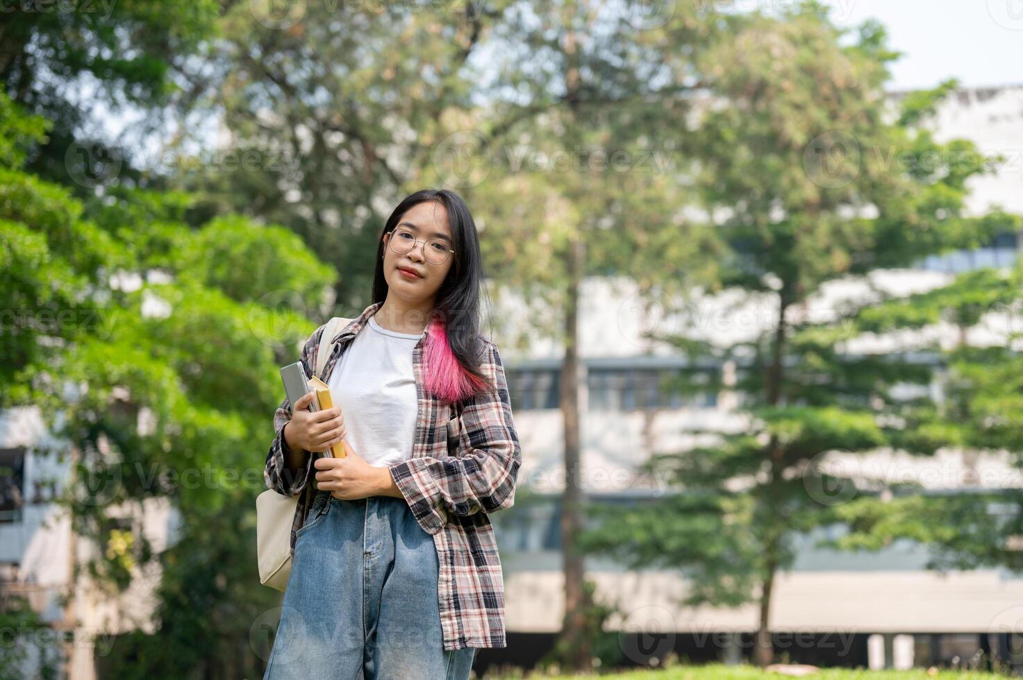 A confident young Asian female college student is looking at the camera while standing in the park. photo