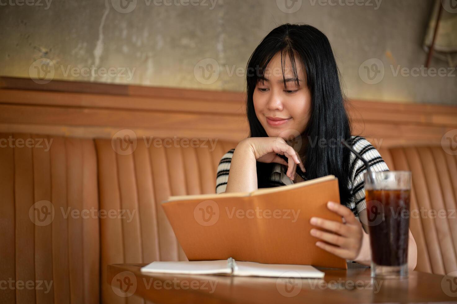 A happy young Asian woman is reading a book or doing homework in a beautiful vintage coffee shop. photo