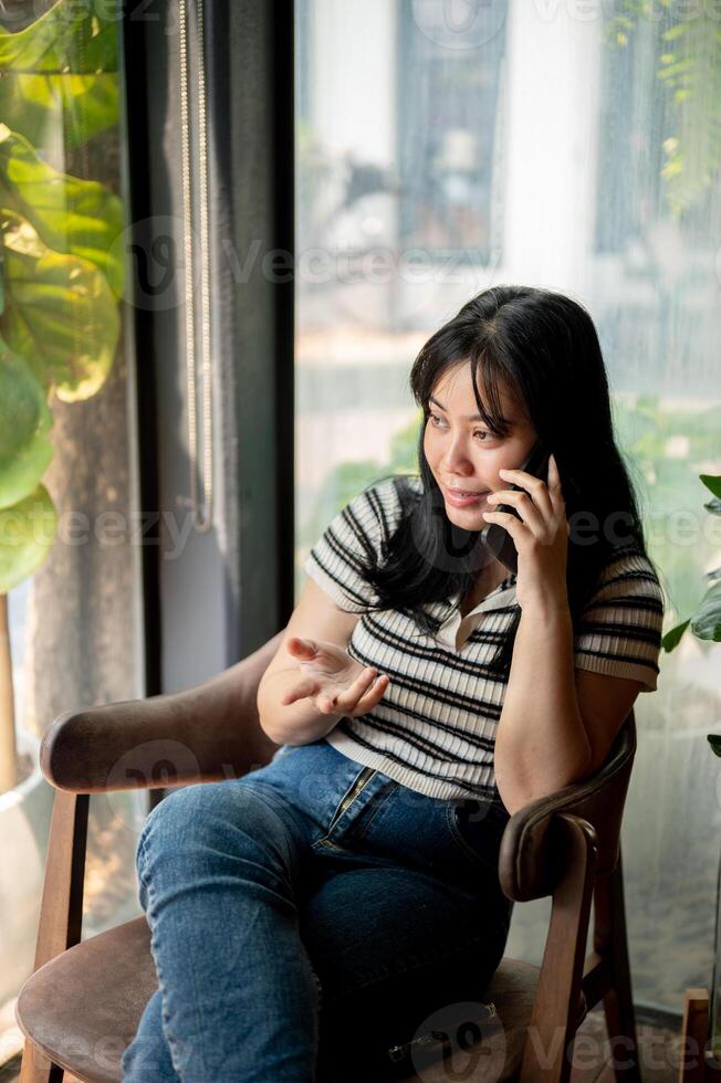 A positive Asian woman is talking on the phone with someone while sitting in a coffee shop. photo