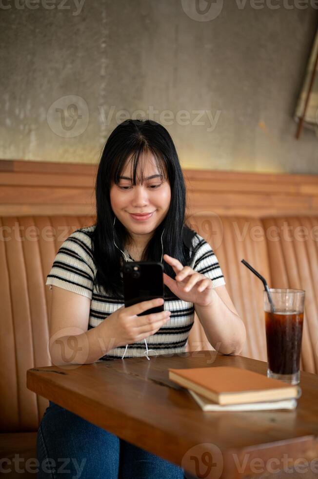 An Asian woman is listening to music on her headphones and using her smartphone in a coffee shop. photo