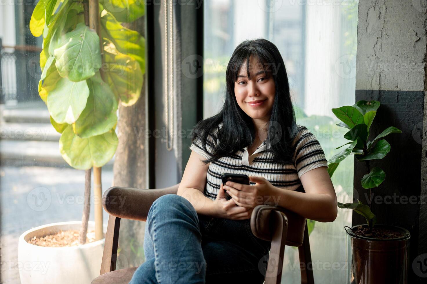 An attractive, smiling Asian woman in casual wear is sitting by the window in a vintage coffee shop. photo