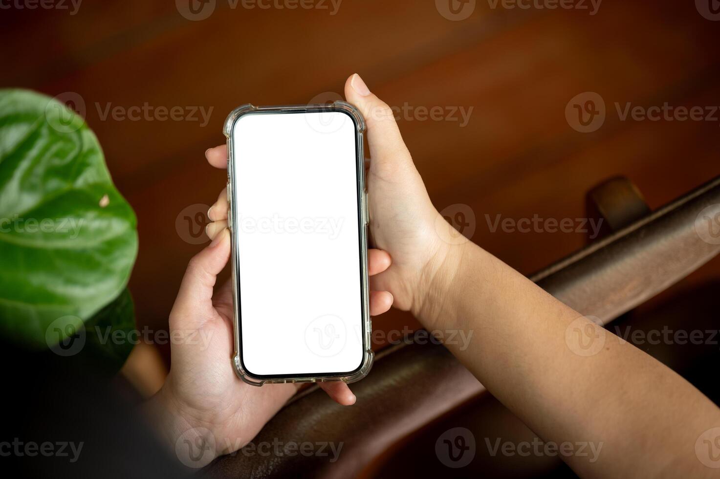 A woman holding a white-screen smartphone mockup over a blurred rustic wood background. photo