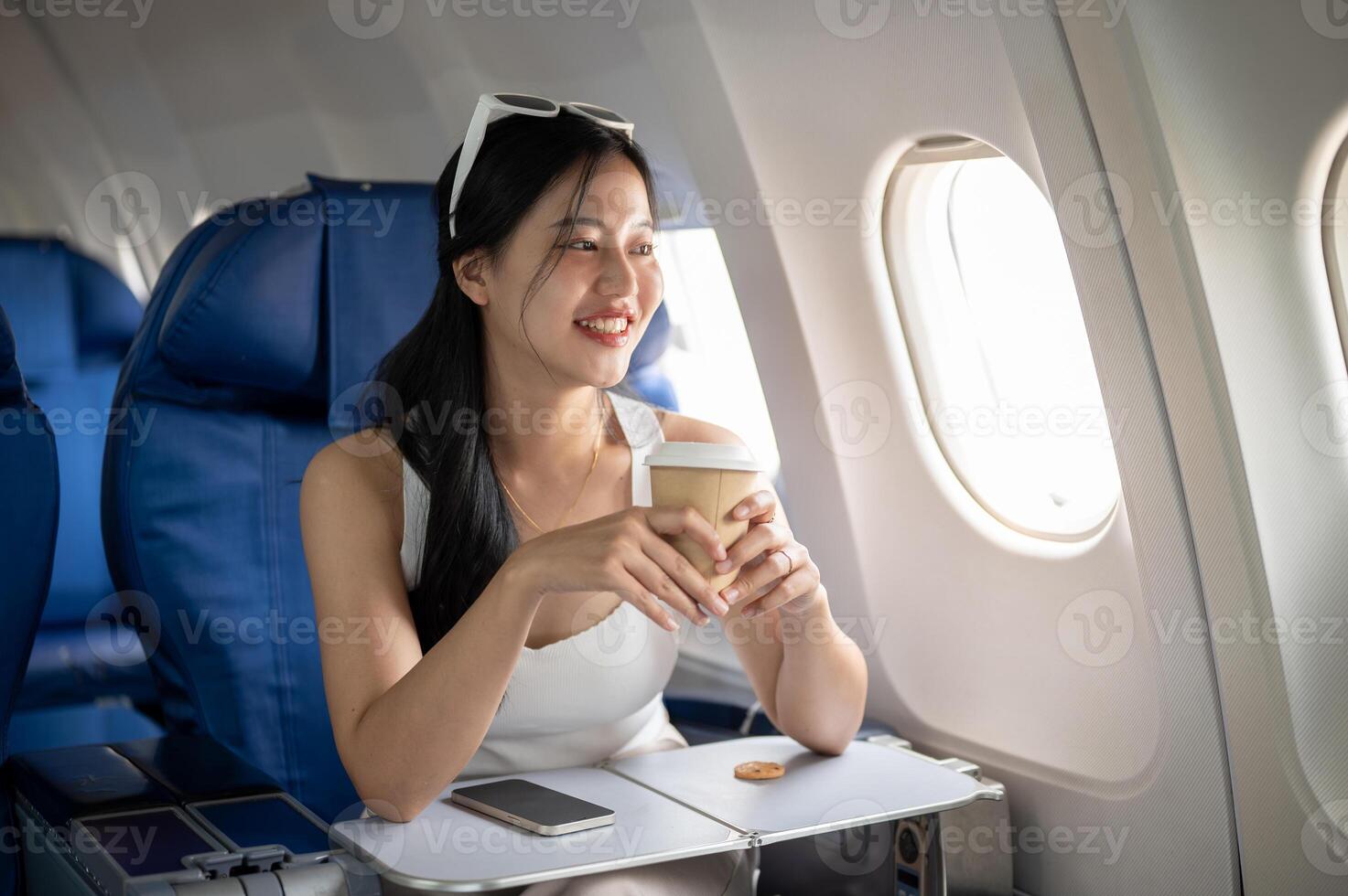 A happy Asian female sipping coffee and enjoying the view outside the window during her flight. photo