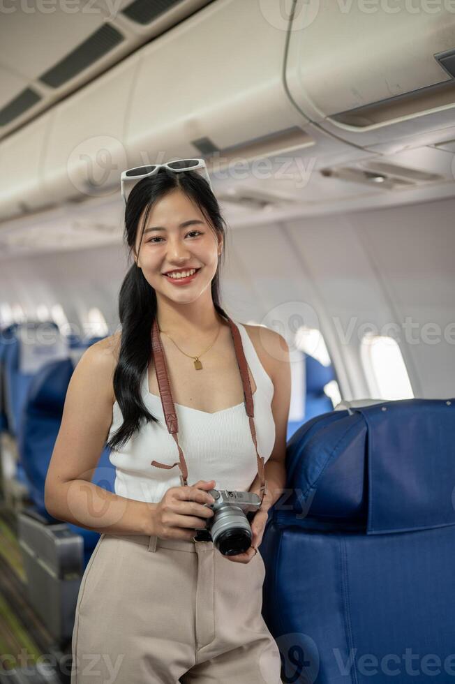 An attractive Asian female passenger stands in the aisle on a plane, smiling at the camera. photo