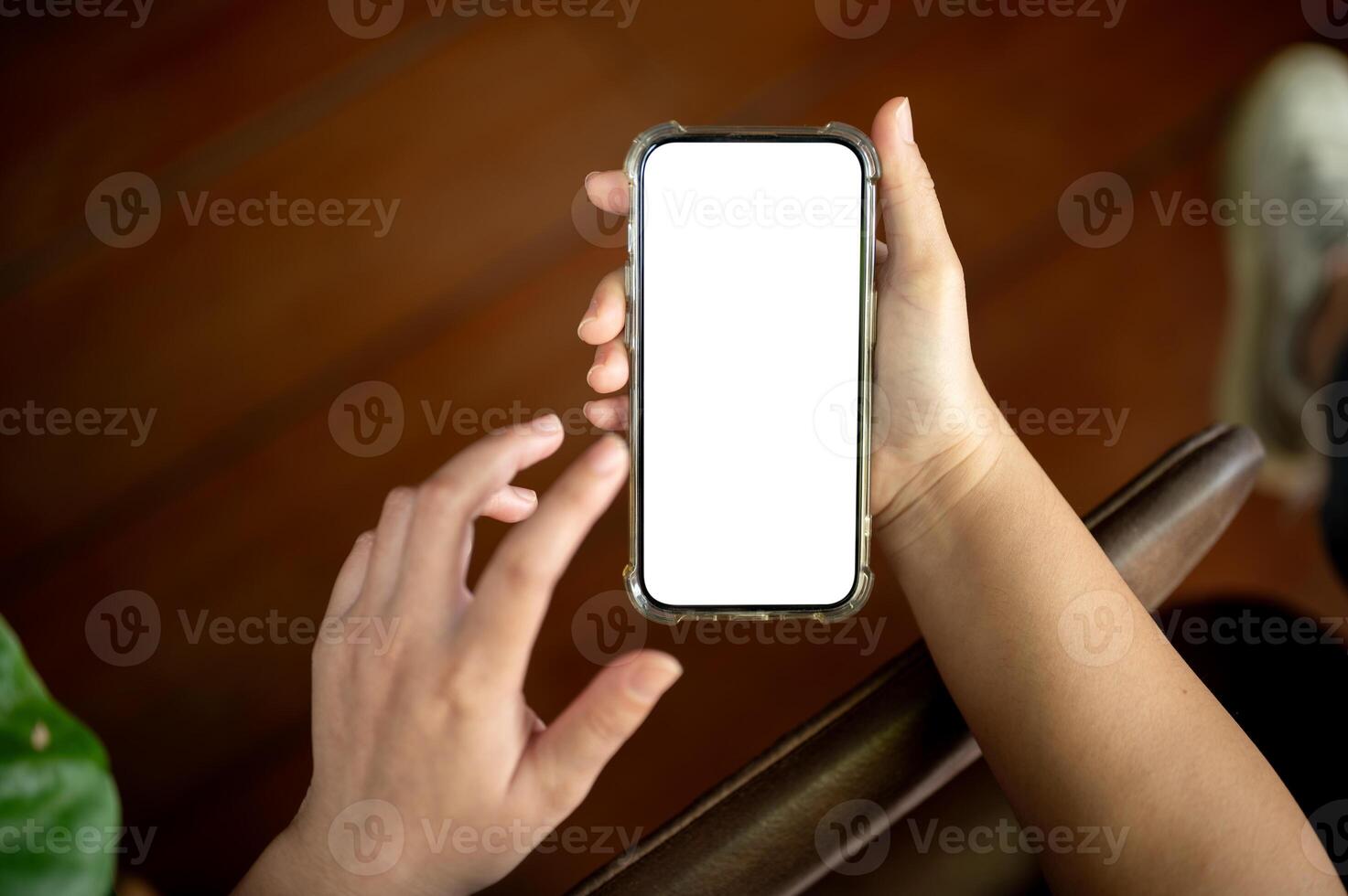 A woman holding a white-screen smartphone mockup over a blurred rustic wood background. photo