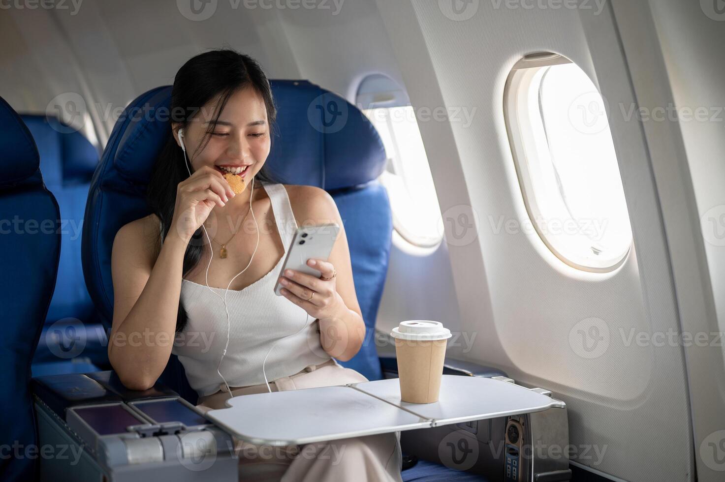 A female passenger is enjoying snacks, listening to music on her headphones during the flight. photo