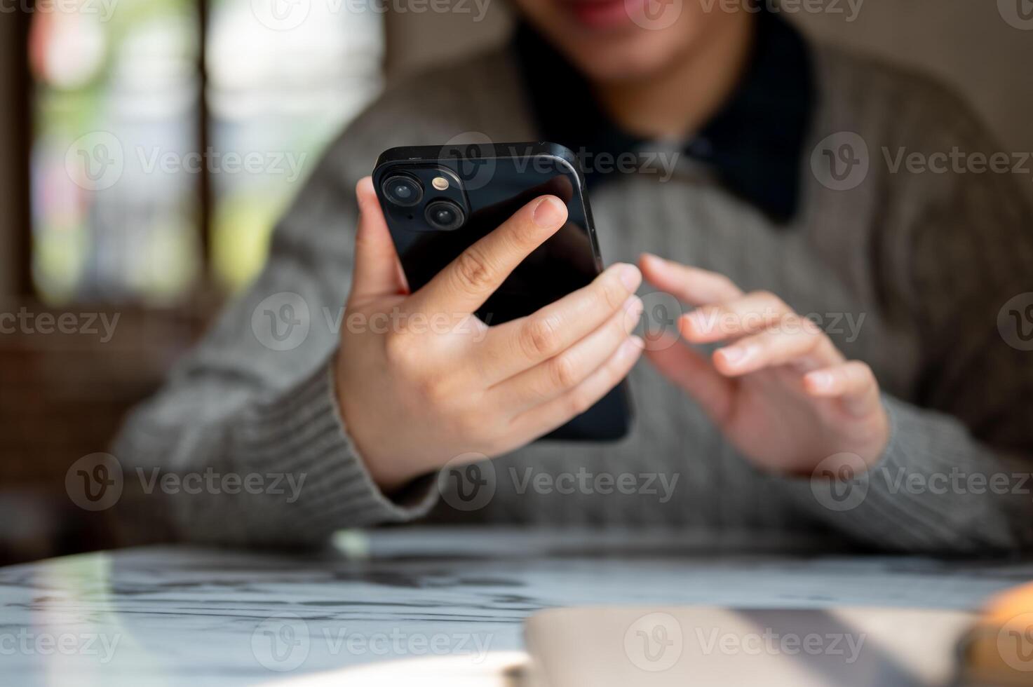 A cropped image of an Asian woman using her smartphone at a table indoors, checking messages photo