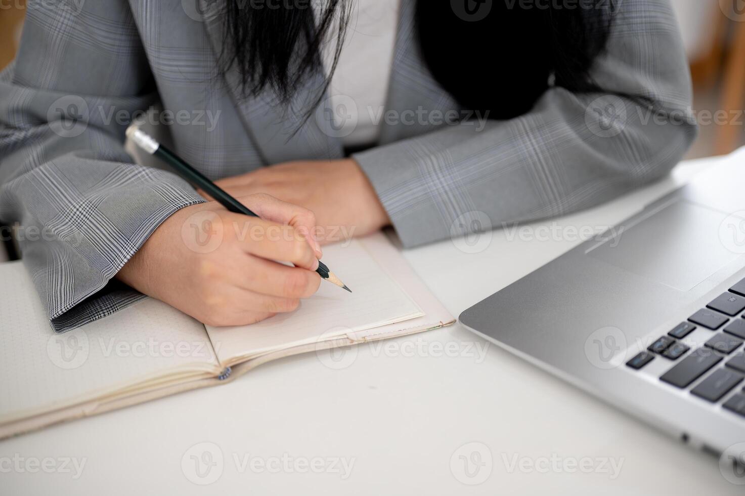 A cropped shot of a businesswoman focused on writing or taking notes in the notebook with a pencil. photo