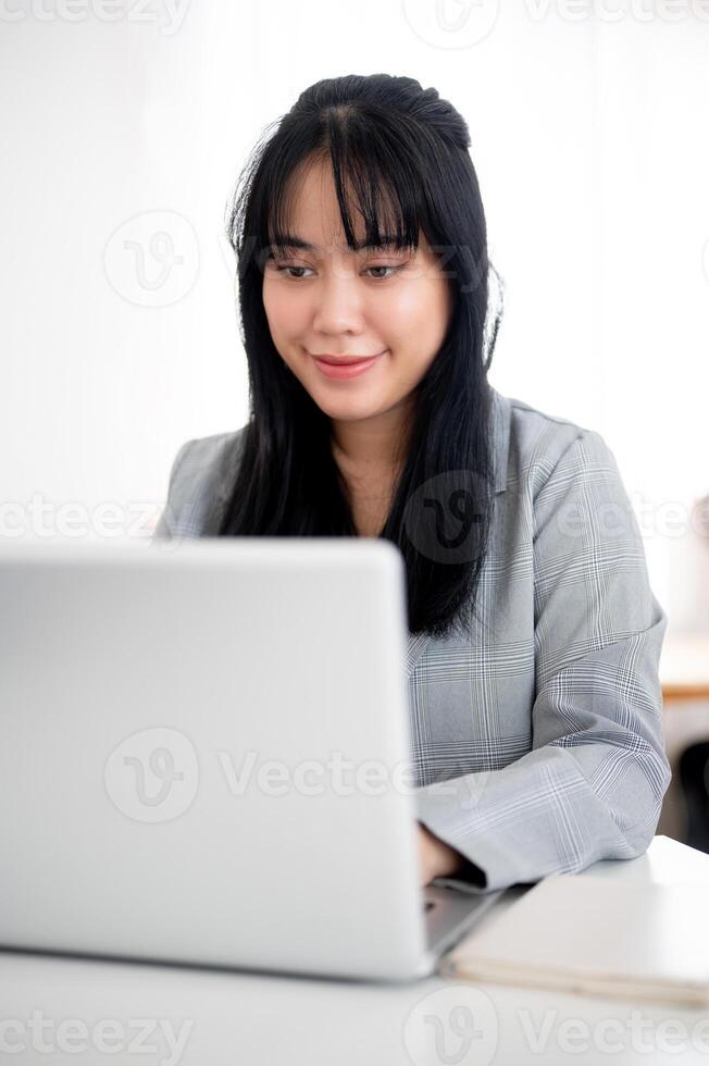 un hermosa asiático mujer de negocios o hembra secretario es trabajando en su ordenador portátil en un moderno oficina. foto