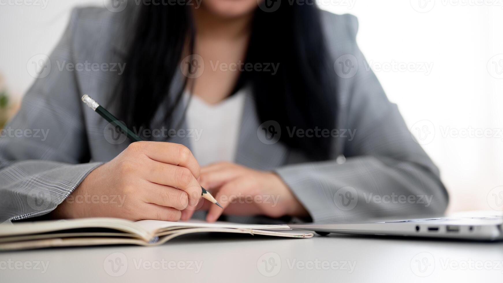 A cropped shot of a businesswoman focused on writing or taking notes in the notebook with a pencil. photo