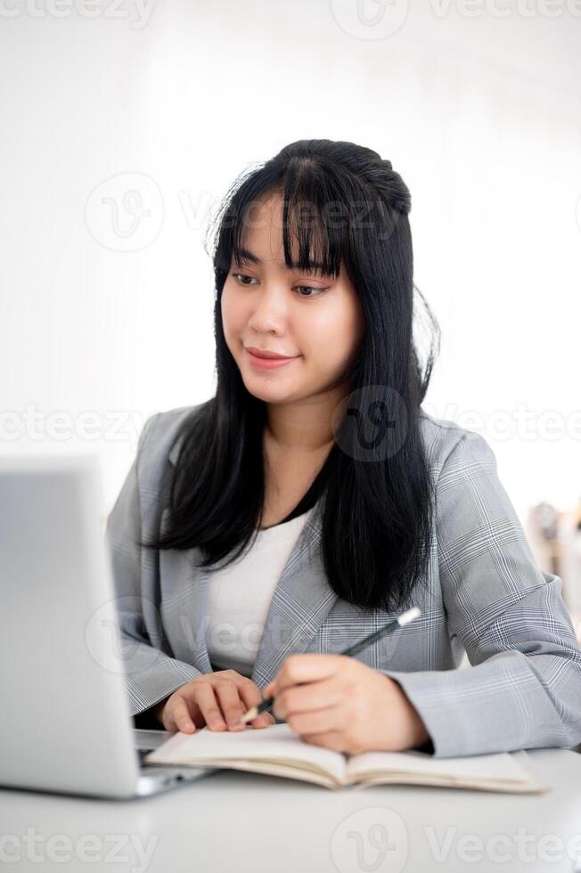 A young Asian businesswoman is looking at her laptop screen while taking notes in the notebook. photo