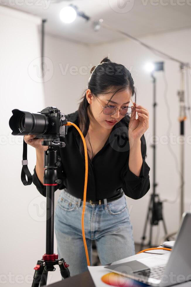 Cool, professional Asian female photographer is checking images on her laptop, working in the studio photo