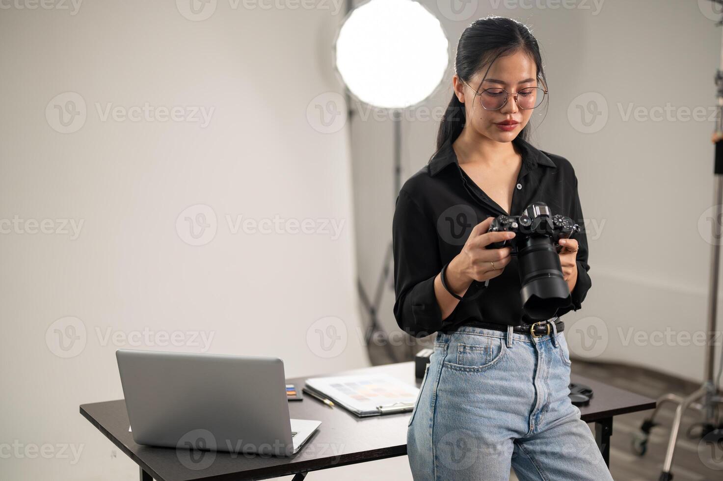 Professional Asian female photographer is focusing on adjusting her DSLR camera, working in a studio photo