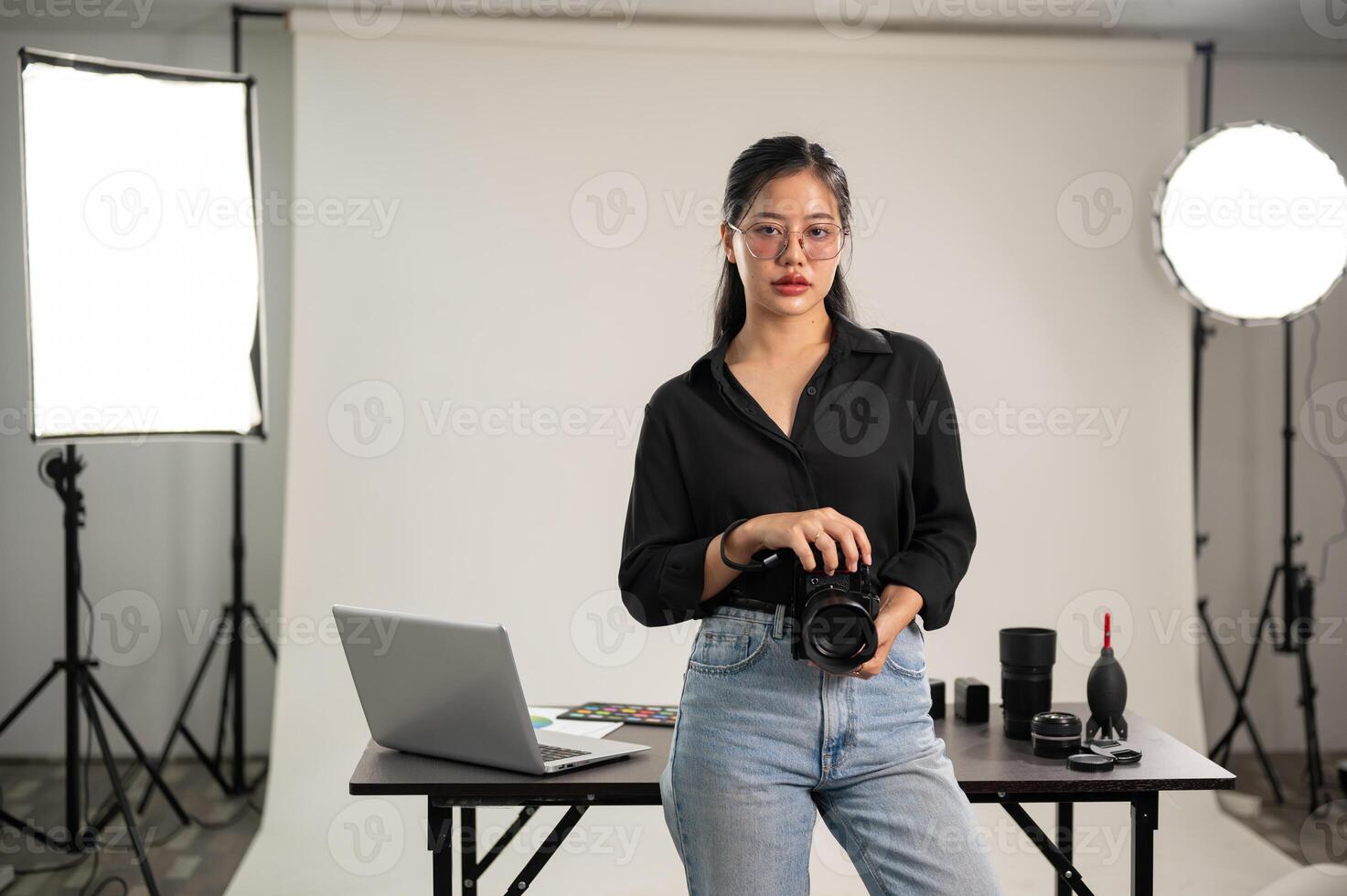 A confident Asian female photographer is standing in her studio with a DSLR camera in her hand. photo