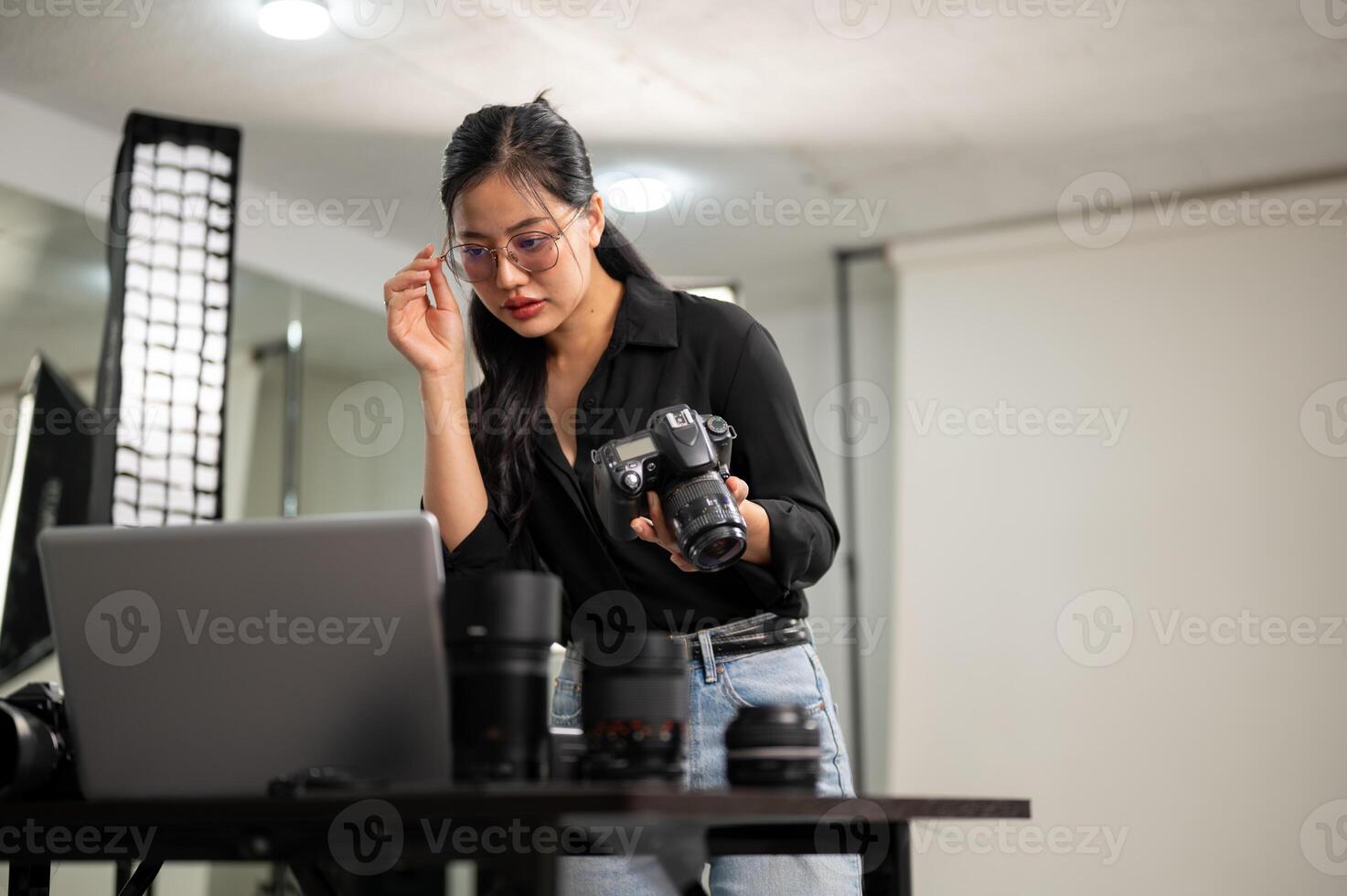 un atractivo asiático hembra fotógrafo es comprobación imágenes en su computadora portátil, trabajando en un estudio. foto