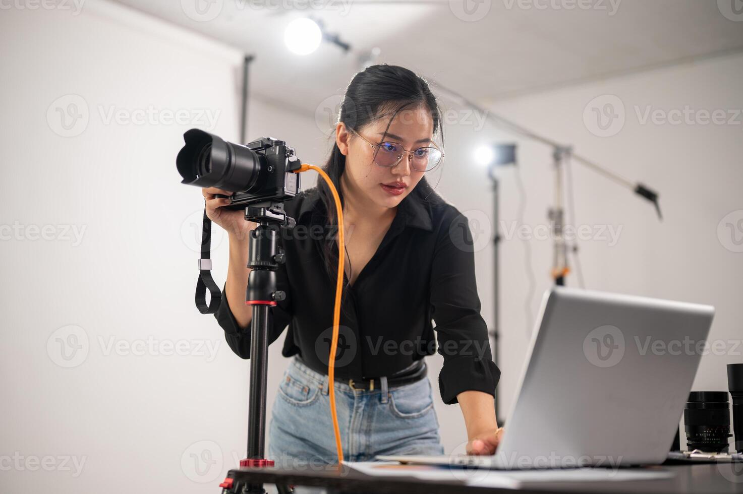 Cool, professional Asian female photographer is checking images on her laptop, working in the studio photo