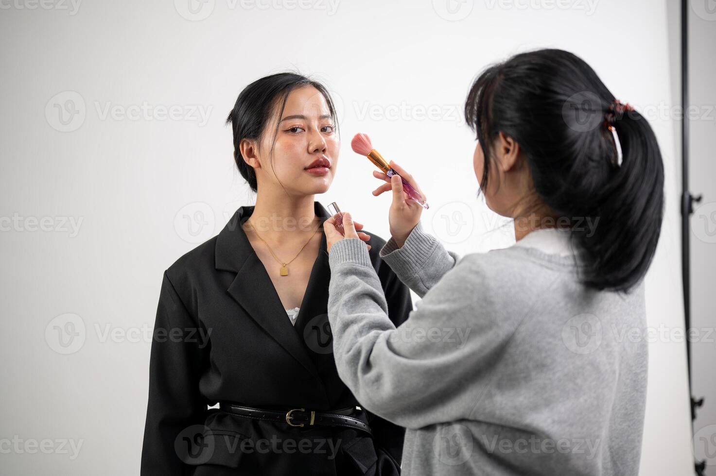 A female model is having makeup applied by a makeup artist, preparing for a photoshoot in the studio photo