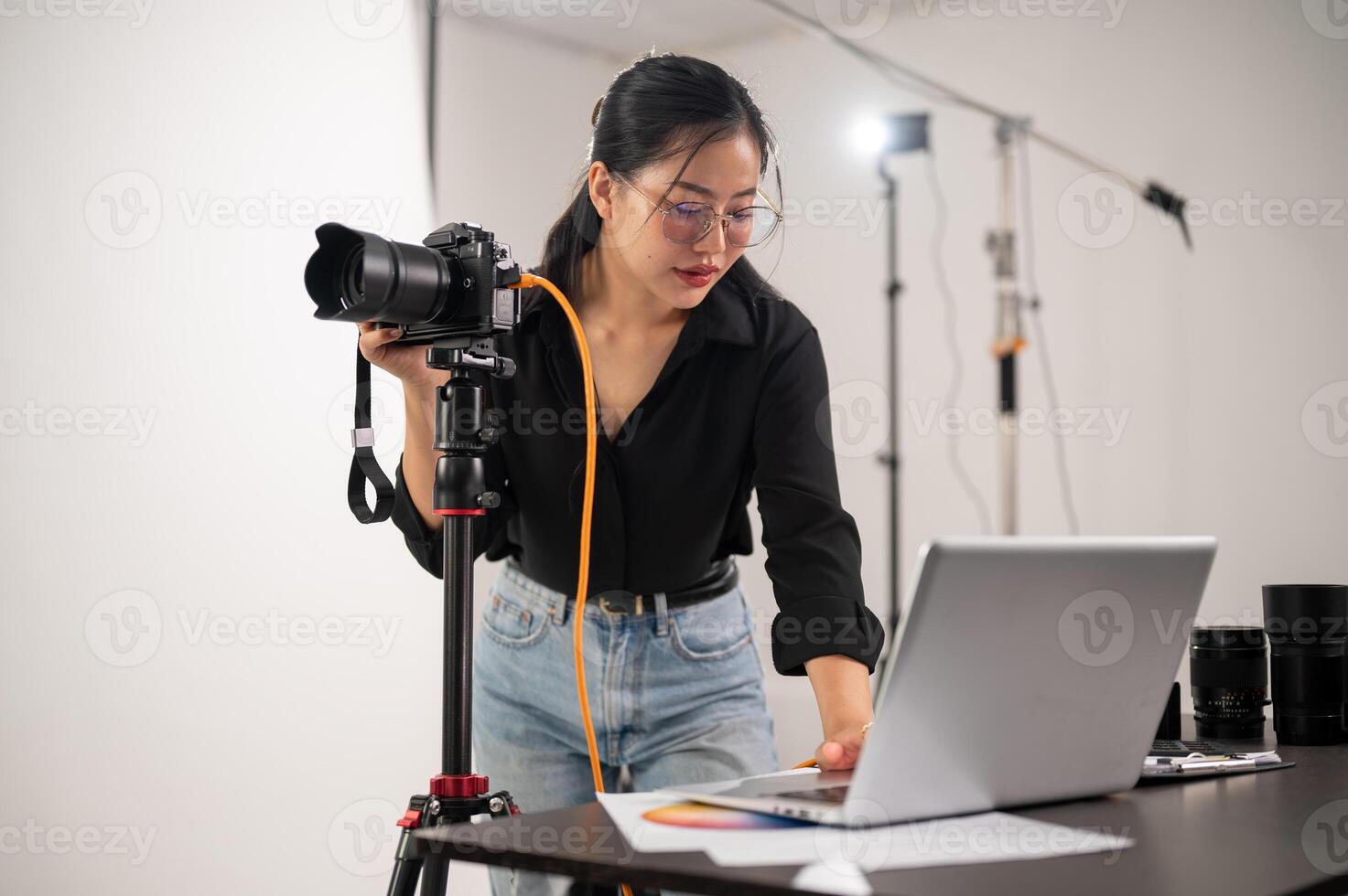 Cool, professional Asian female photographer is checking images on her laptop, working in the studio photo