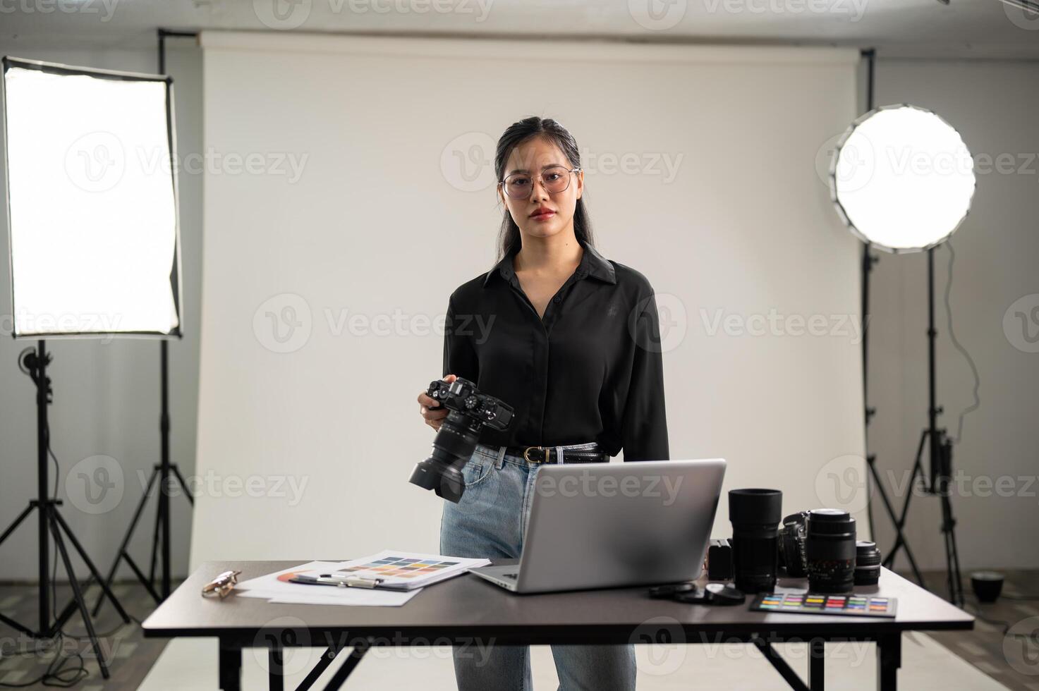 A young, confident Asian female photographer with her DSLR camera in a professional studio. photo