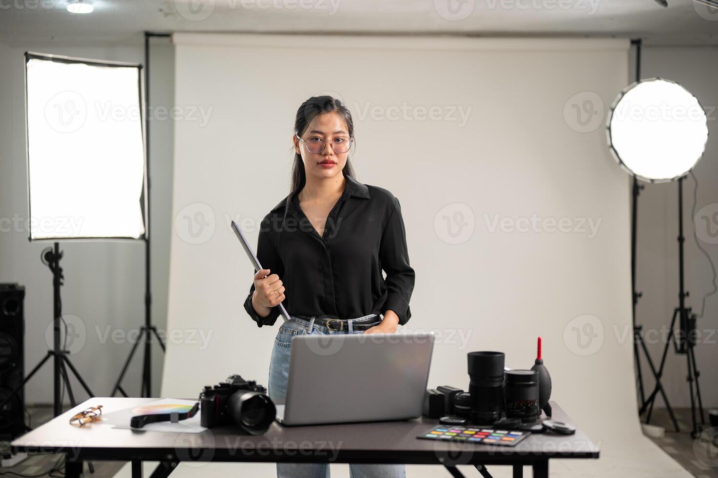 An elegant Asian female photographer in a black shirt is standing in her photoshoot studio. photo