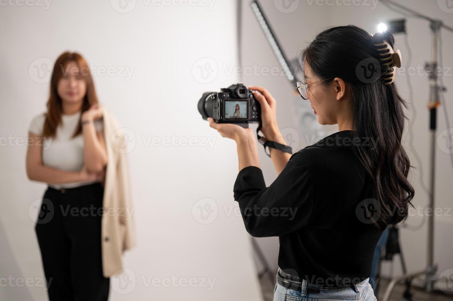A professional, cool Asian female photographer taking pictures of a model in the studio. photo