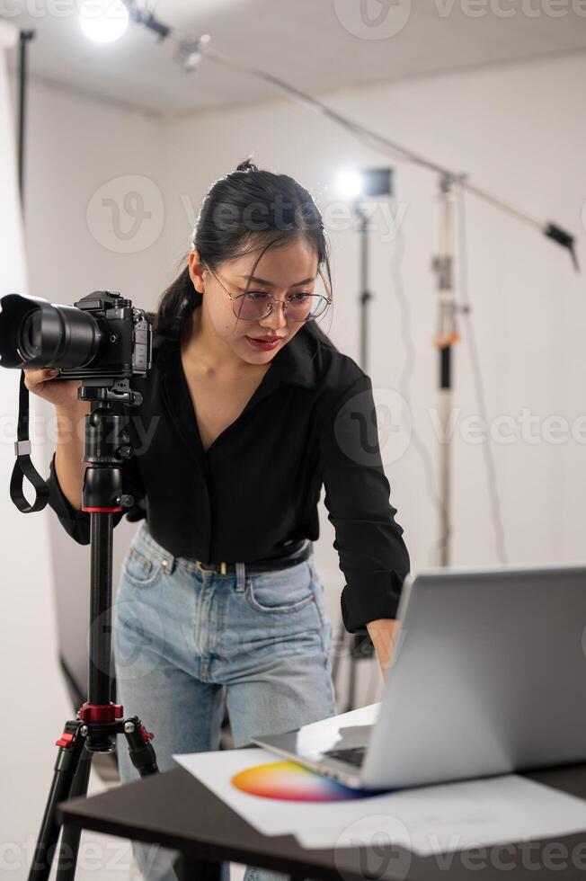 Cool, professional Asian female photographer is checking images on her laptop, working in the studio photo