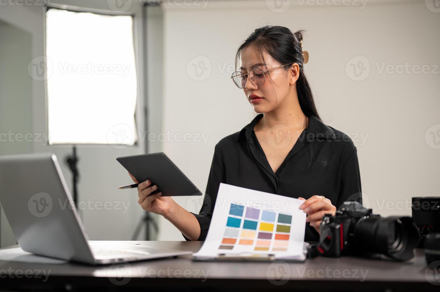Professional Asian female photographer is looking at a color checker, working in a photoshoot studio photo