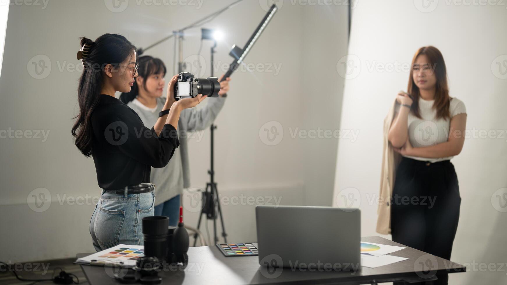 A professional, cool Asian female photographer taking pictures of a model in the studio. photo