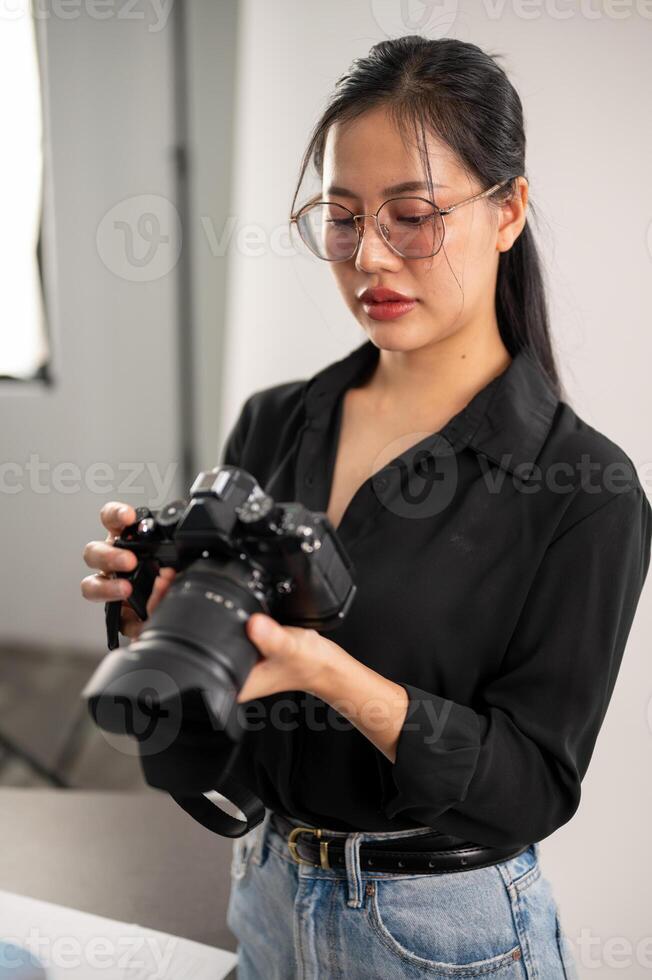 A confident, experienced Asian female photographer is adjusting her DSLR camera, preparing photoshoot equipment, and working in the studio. photo