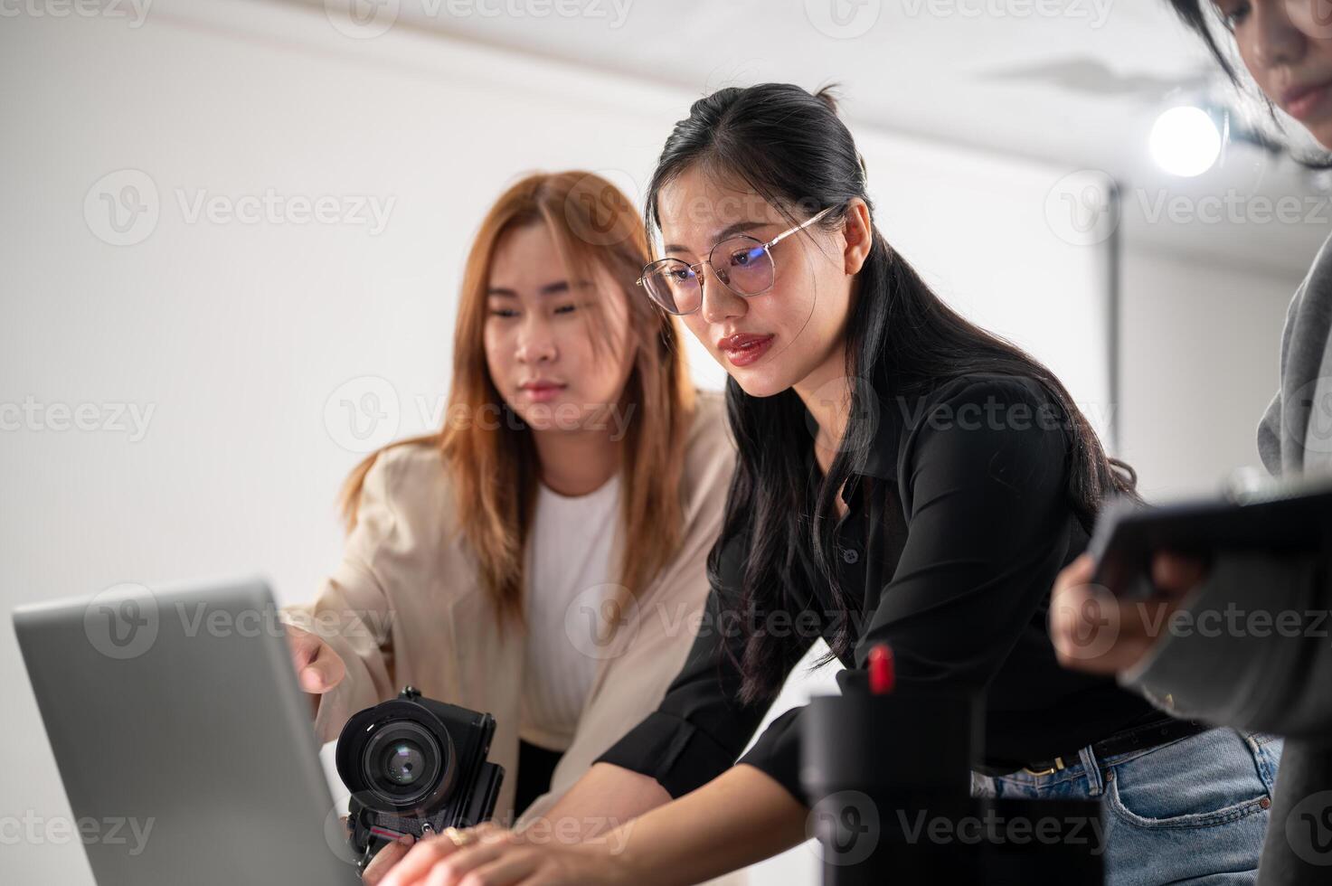 un profesional asiático hembra fotógrafo es trabajando con su asistentes en un Sesión de fotos estudio.