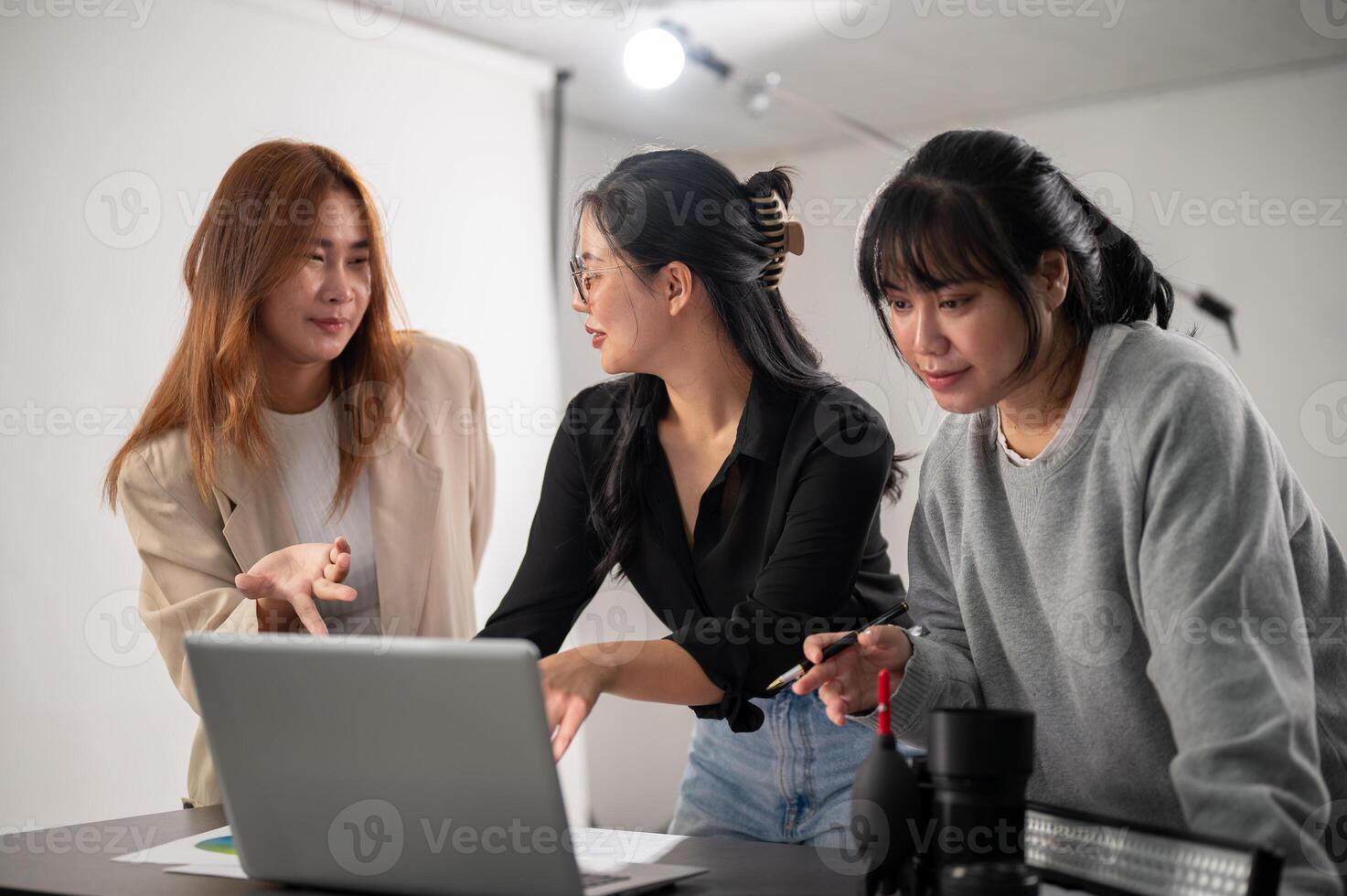 A female photographer is checking images on her laptop and working in the studio with her assistants photo