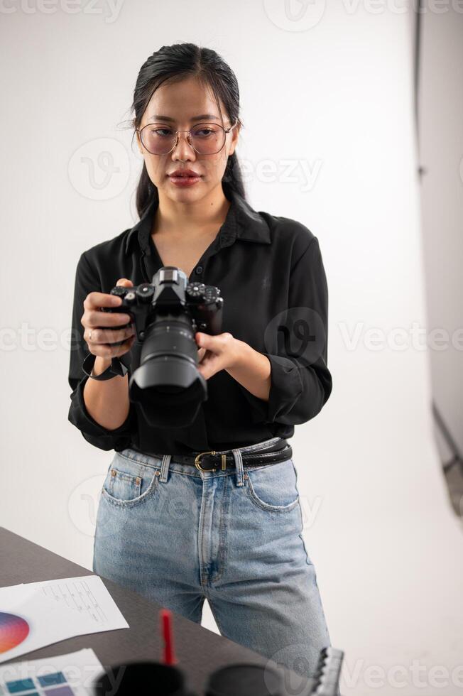 A confident, experienced Asian female photographer is adjusting her DSLR camera, preparing photoshoot equipment, and working in the studio. photo