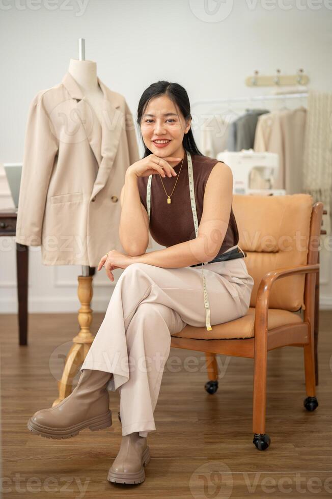 An attractive Asian female fashion designer is sitting on an armchair in her atelier studio. photo