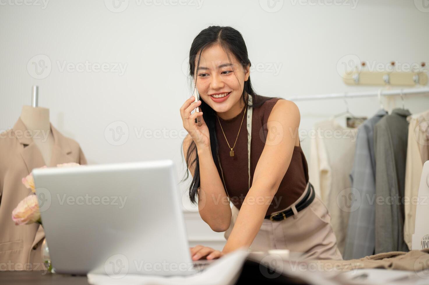 A professional, busy female tailor is talking on the phone with while working in her studio. photo