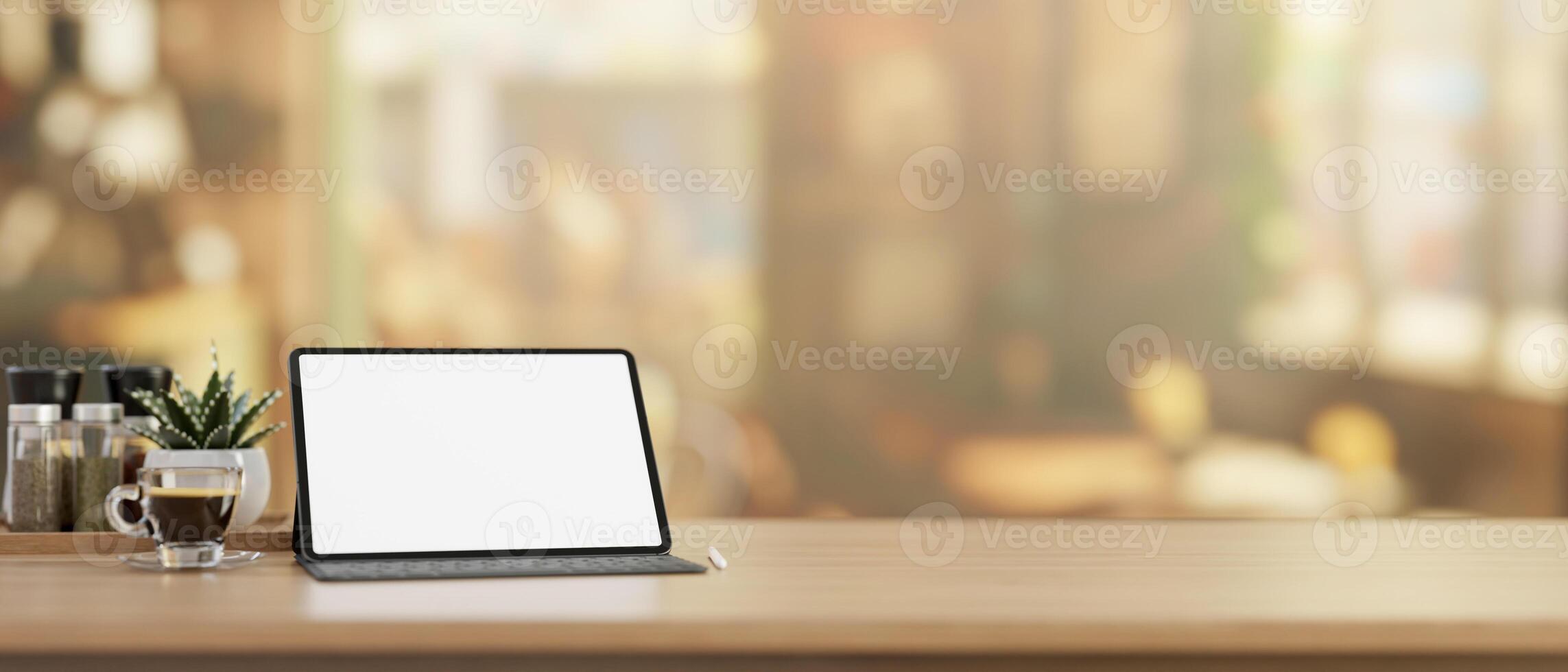 A digital tablet mockup with a wireless keyboard on a wooden tabletop in a cosy, bright coffee shop. photo