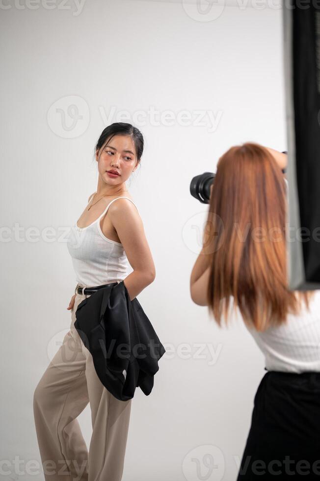 A professional photographer is taking pictures of an attractive young Asian female model in a studio photo