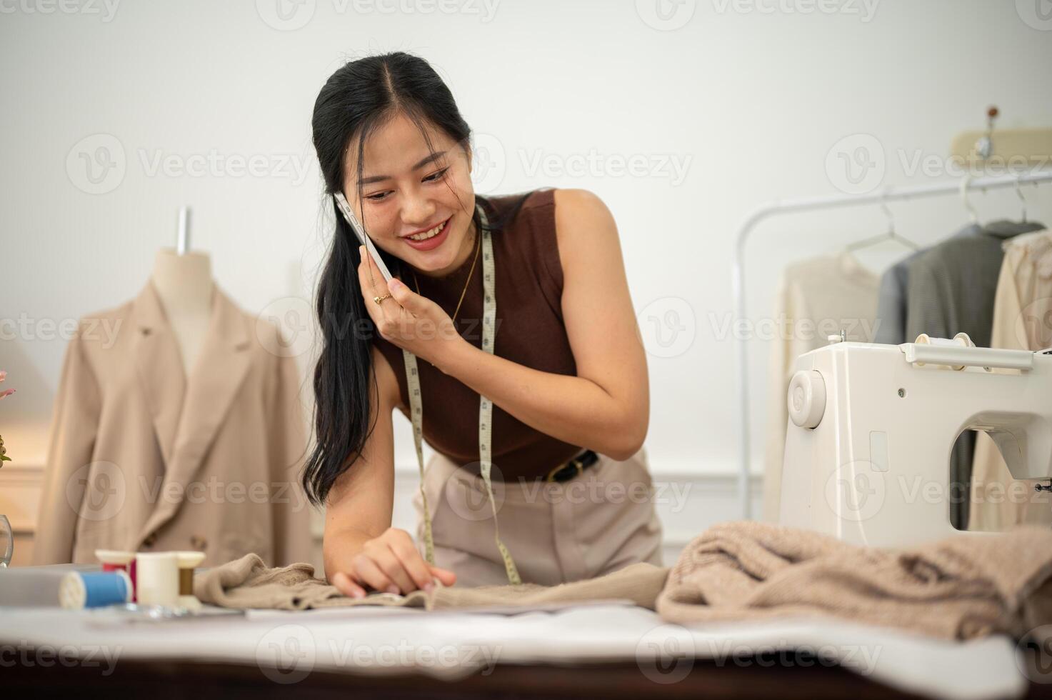 A professional, busy female tailor is talking on the phone with while working in her studio. photo